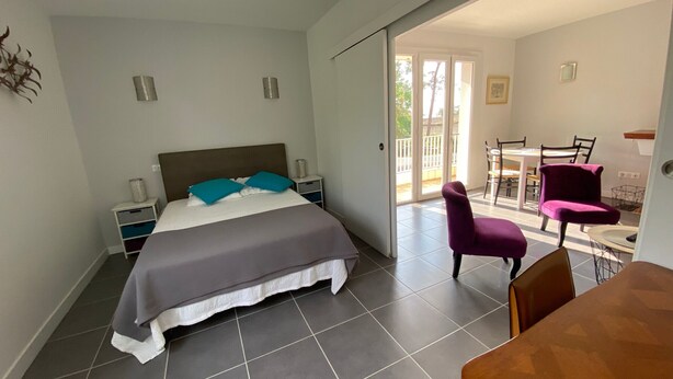 A bedroom with a bed, a nightstand, a chair, and a table. There is a sliding door leading to a balcony.