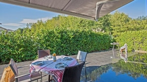An outdoor dining area with a table set for two, surrounded by lush greenery and a clear glass pool. - Villa Jardins de la Mer (Poggio-Mezzana)