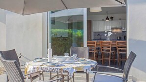 An outdoor dining area with a table set for two, surrounded by wicker chairs, and a large umbrella providing shade. - Villa Jardins de la Mer (Poggio-Mezzana)