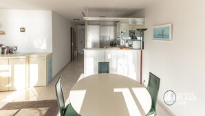 Een moderne keuken met witte kasten, een eethoek met een ronde tafel en stoelen, en uitzicht op de aangrenzende woonruimte.