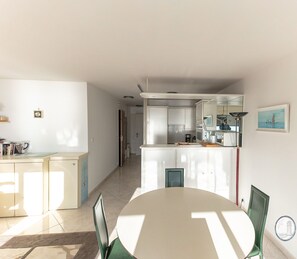 A modern kitchen with white cabinets, a dining area with a round table and chairs, and a view of the adjacent living space.