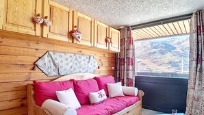 Acogedora habitación de cabaña de madera con sofá de madera, una mesita con vasos y una ventana con cortinas.