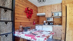 Un interior de madera con una mesa de comedor para cuatro, una zona de cocina con microondas y estufa, y un adorno rojo en la pared.