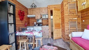 Una cabaña de madera compacta con comedor, kitchenette y una cama.