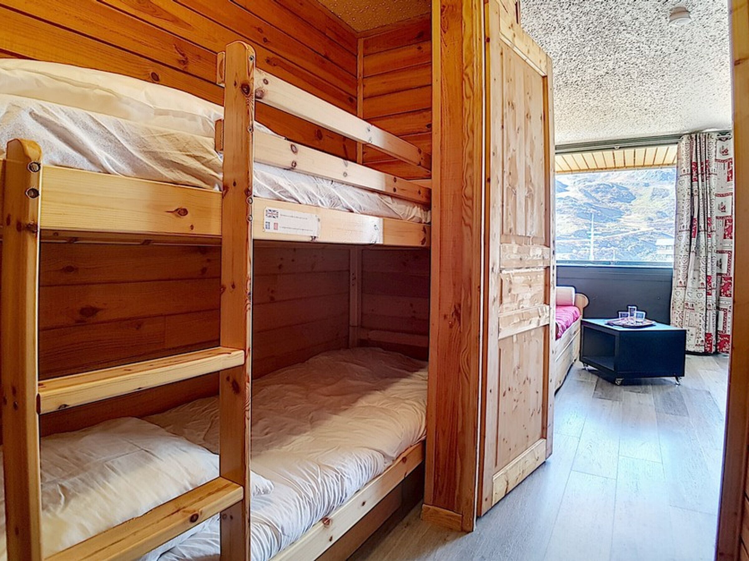 Quarto com beliche de madeira, uma pequena mesa e vista para as montanhas.