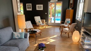 A living room with a grey sofa, striped chairs, a wooden coffee table with a flower, and a TV stand. - Homerez - Villa Soulac-sur-Mer (Soulac-sur-Mer)