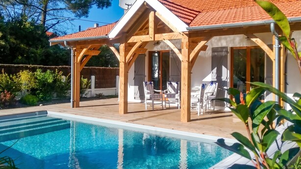 A poolside area with a wooden pergola, lounge chairs, and a clear blue pool. - Homerez - Villa Soulac-sur-Mer (Soulac-sur-Mer)