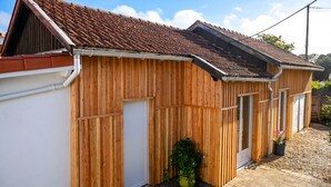 A wooden building with a tiled roof, a door, and a small garden area with potted plants. - Homerez - Villa Soulac-sur-Mer (Soulac-sur-Mer)