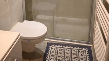 Une cabine de douche fermée par des parois en verre, avec des toilettes et un porte-serviettes.