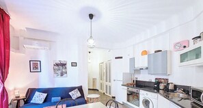 Un espacio habitable compacto con kitchenette, comedor y sofá con cojines.