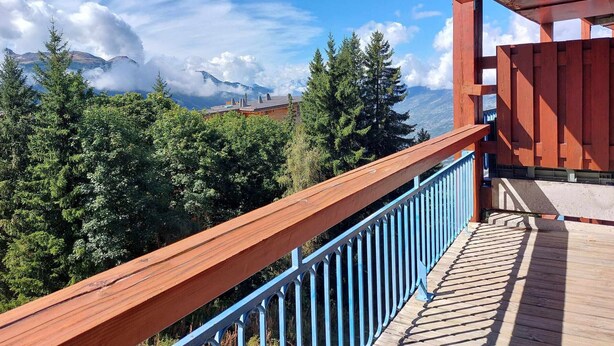 Una terraza de madera con barandilla azul que da a una zona montañosa boscosa.