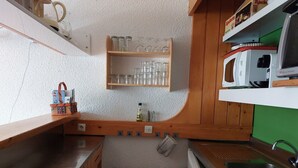Cocina compacta con muebles de madera, microondas, pileta y una alacena con cristalería.