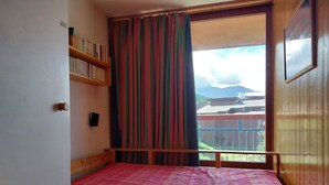 Un dormitorio con cama, una estantería, una ventana con cortinas y vistas a montañas.