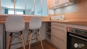 A modern kitchen with wooden cabinets, a built-in oven, and two white chairs. - Renovated 66m² apartment, 1 bedroom, sea view, 4th floor, fiber, 3 stars (Les Sables-d'Olonne)