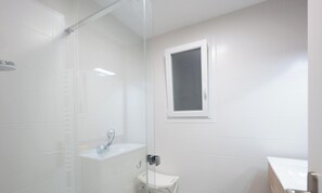 Une salle de bain moderne avec une douche à parois de verre, une petite fenêtre et un lavabo blanc.