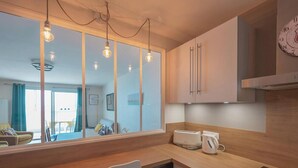 A modern kitchen with wooden cabinets, a built-in oven, and a window overlooking a balcony. - Renovated 66m² apartment, 1 bedroom, sea view, 4th floor, fiber, 3 stars (Les Sables-d'Olonne)