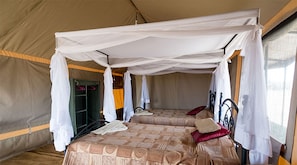 A tented room with two beds, each with a canopy. There is a wardrobe and a hanging chair visible. - Serengeti Wild Camps (Serengeti)
