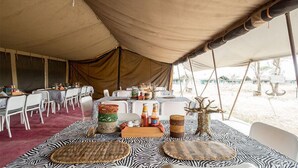 A tented dining area with tables set for meals, featuring zebra-patterned mats and various food items. - Serengeti Wild Camps (Serengeti)