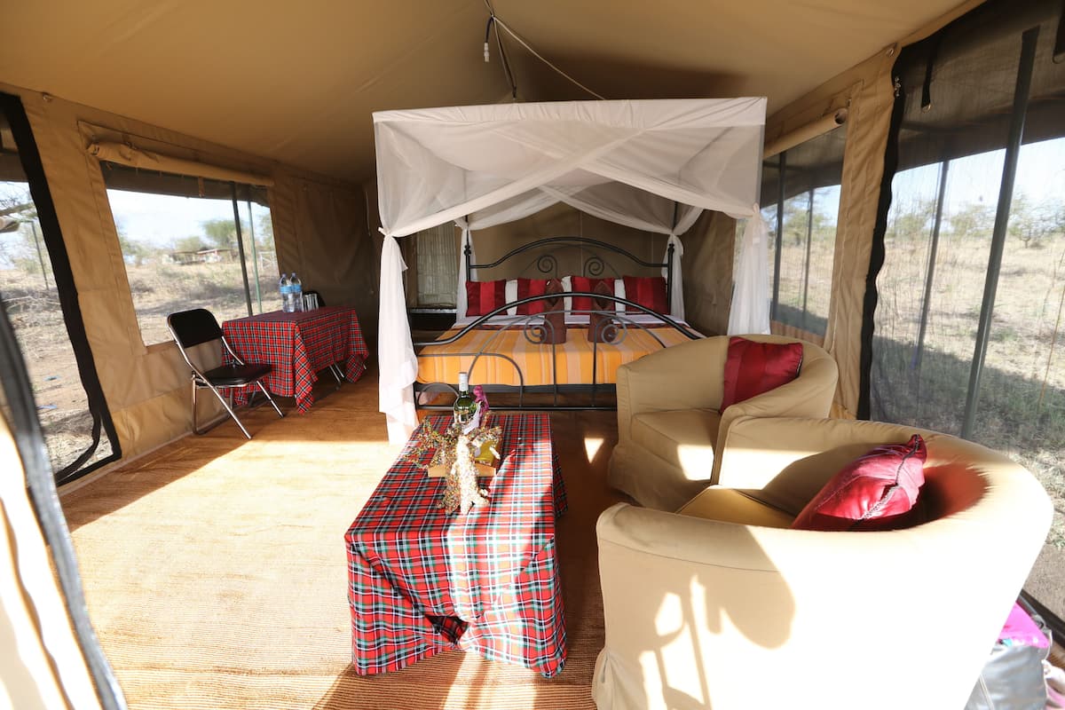 Un hébergement sous tente comprenant un lit, une table recouverte d’une nappe à carreaux rouges et une chaise.