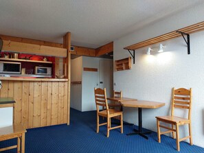 Una cucina compatta con mobili in legno, un forno a microonde e un appendiabiti. C'è un'area pranzo con un tavolo e due sedie.