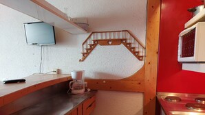A compact kitchen with a wooden counter, a coffee maker, a microwave, and a red stove.