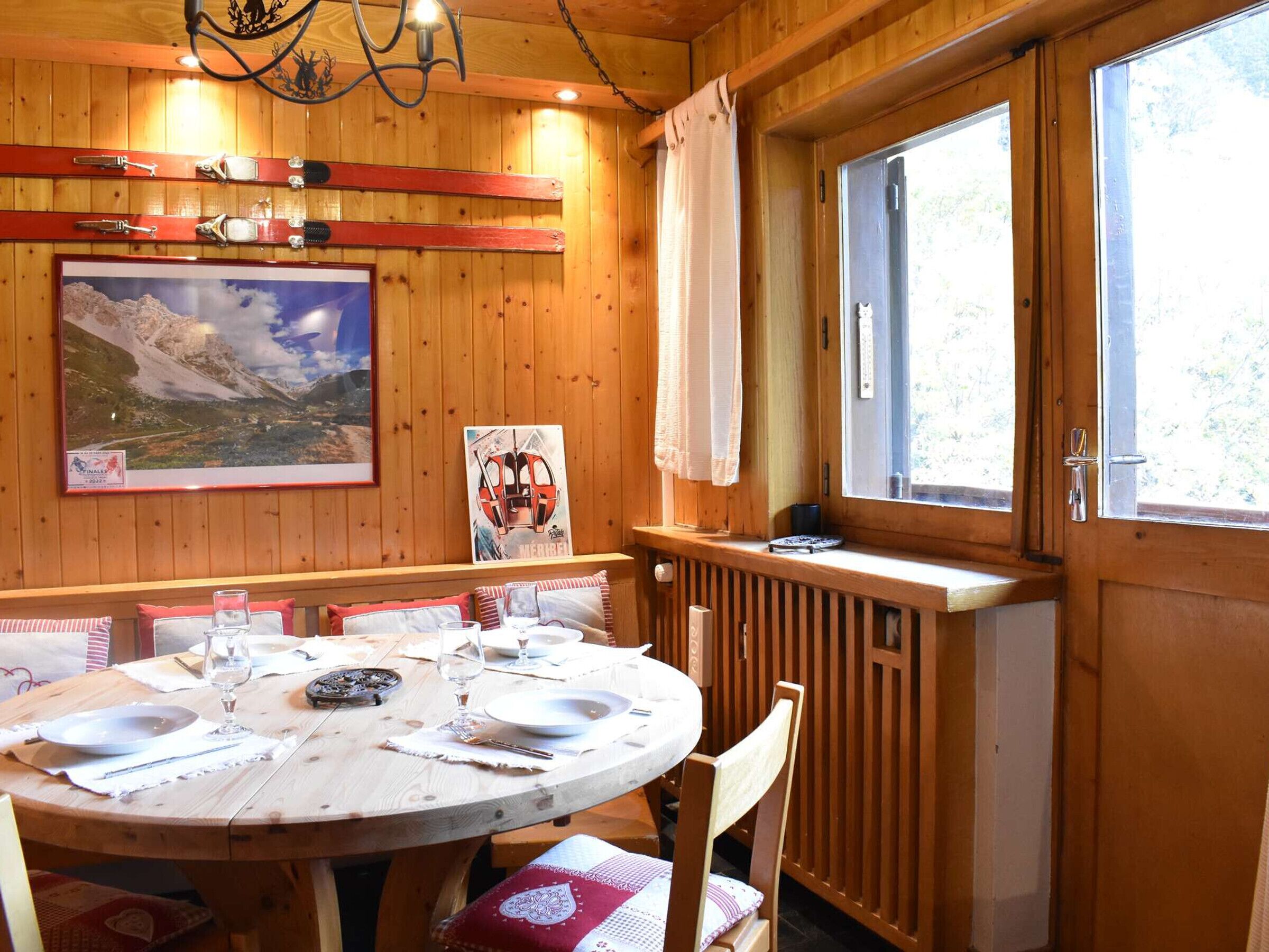 Ein Holzinterieur mit einem runden Esstisch, gedeckt für vier Personen, einem Gemälde von einer Berglandschaft und einem Fenster mit Blick auf Bäume.
