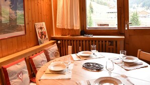 A wooden interior with a dining table set for two, a window with a view of a mountainous landscape, and a radiator below the window. - 2-room apartment for 5 at Méribel slopes (Méribel)