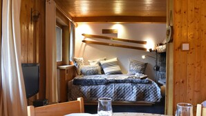 A cozy wooden cabin room with a bed, a table set for dining, and a television. - 2-room apartment for 5 at Méribel slopes (Méribel)