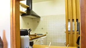 A kitchen with a stove, oven, and a black range hood. There are white tiles on the wall and a wooden counter with cups and spoons. - 2-room apartment for 5 at Méribel slopes (Méribel)