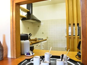 A kitchen with a stove, oven, and a black range hood. There are white tiles on the wall and a wooden counter with cups and spoons.