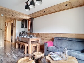 A cozy living room with a wooden floor, a grey sofa, a dining table set with dishes, and a coffee machine. - Beautiful renovated 4-room duplex - Ski-in/Ski-out - Balcony (Les Menuires)