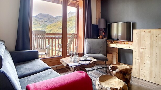 A cozy room with a wooden ceiling, a large window with a mountain view, a TV, and a seating area with a table and chairs.