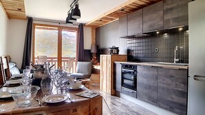 A modern kitchen with a wooden ceiling, a dining area with a table set for four, and a view of the outdoors through large windows.