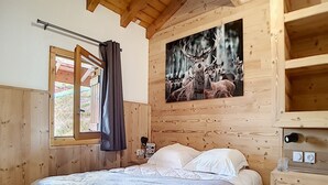 A wooden cabin bedroom with a bed, a window with curtains, and a wall-mounted picture of deer.