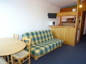 Una habitación con un sofá de madera, una mesa redonda y un televisor montado en la pared.