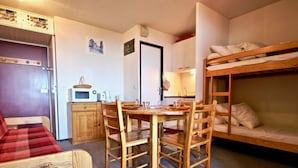 Habitación compacta con literas, una mesa de comedor con sillas, microondas y refrigerador.