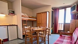Una habitación compacta con una litera, un pequeño kitchenette, una mesa de comedor con sillas y un sofá.