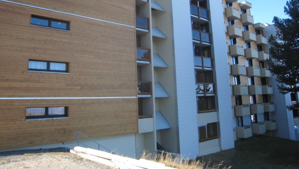 Un edificio moderno de varios pisos con una combinación de paredes de madera y blancas, con balcones y ventanas amplias.