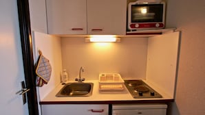Una kitchenette compacta con un lavamanos, una estufa pequeña y un microondas.