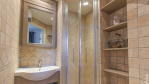 Un baño con lavamanos, espejo, cabina de ducha y estantes con artículos de aseo.