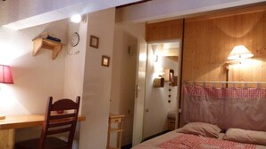 Een slaapkamer met een bed, een stoel, een bureau en een houten garderobe.