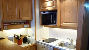 Een kleine keuken met houten kastjes, een Bosch vaatwasser, een magnetron en een spoelbak.