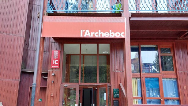 De ingang van een gebouw met een rode gevel en het bord 'l'Archeboc'.