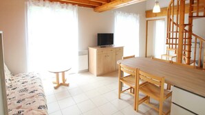 Een gezellige kamer met een houten plafond, een televisie op een kast, een eettafel met stoelen en een trap.