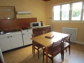 Una cocina compacta equipada con microondas, estufa y armarios. Cuenta con una mesa de comedor con sillas y una ventana con persianas.