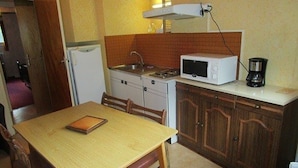 A compact kitchen with a dining table, chairs, a microwave, a coffee maker, and a refrigerator.