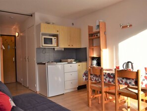 Una cocina funcional con microondas, estufa y armarios de madera. Hay una zona de comedor con mesa y sillas, y un sofá en primer plano.