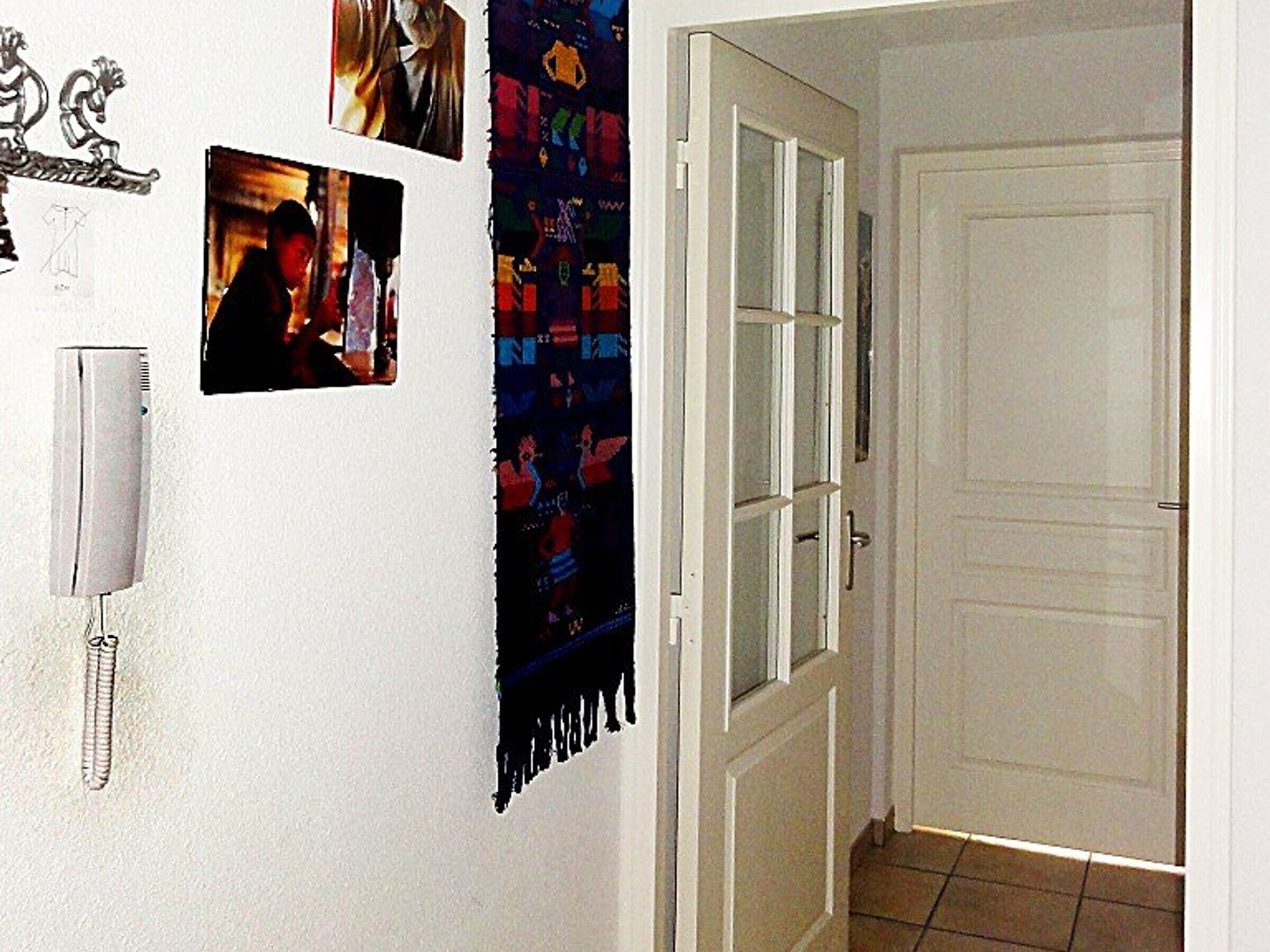 Een hal met een witte deur, een luchtzuiveraar aan de muur en een wandtapijt met een kleurrijk patroon.