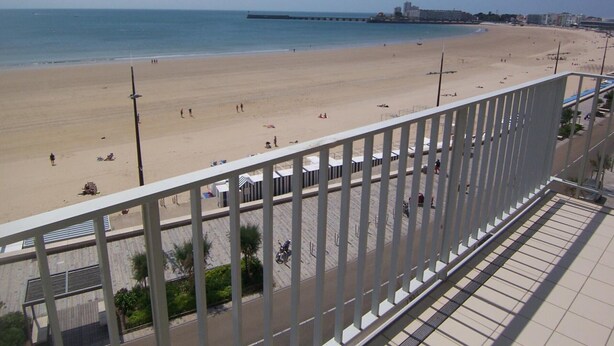 Una playa con vista despejada al mar, un muelle a lo lejos y un edificio de techo plano.