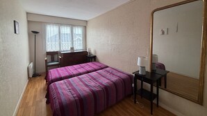 Un dormitorio con dos camas, un escritorio, una silla, una lámpara, un espejo grande y una ventana con cortinas de encaje.
